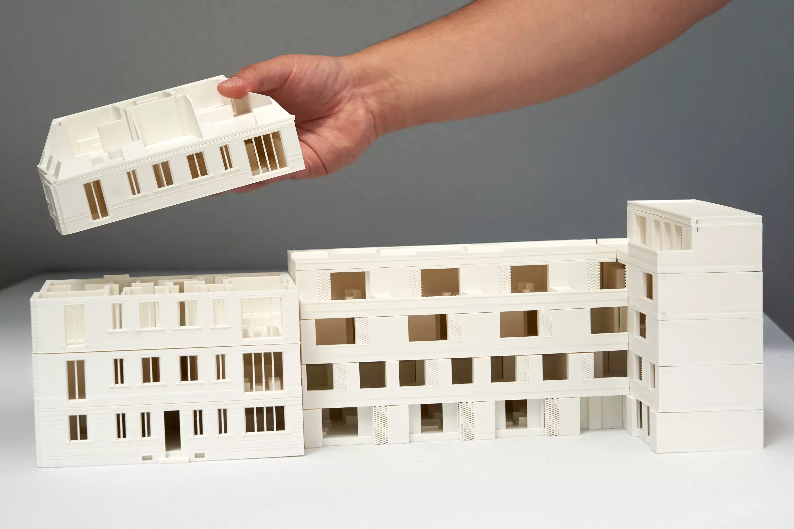 Frontansicht eines modularen 3D-gedruckten Wohnblocks in München, bei dem das Dach gerade abgenommen wird, um das Innenleben sichtbar zu machen